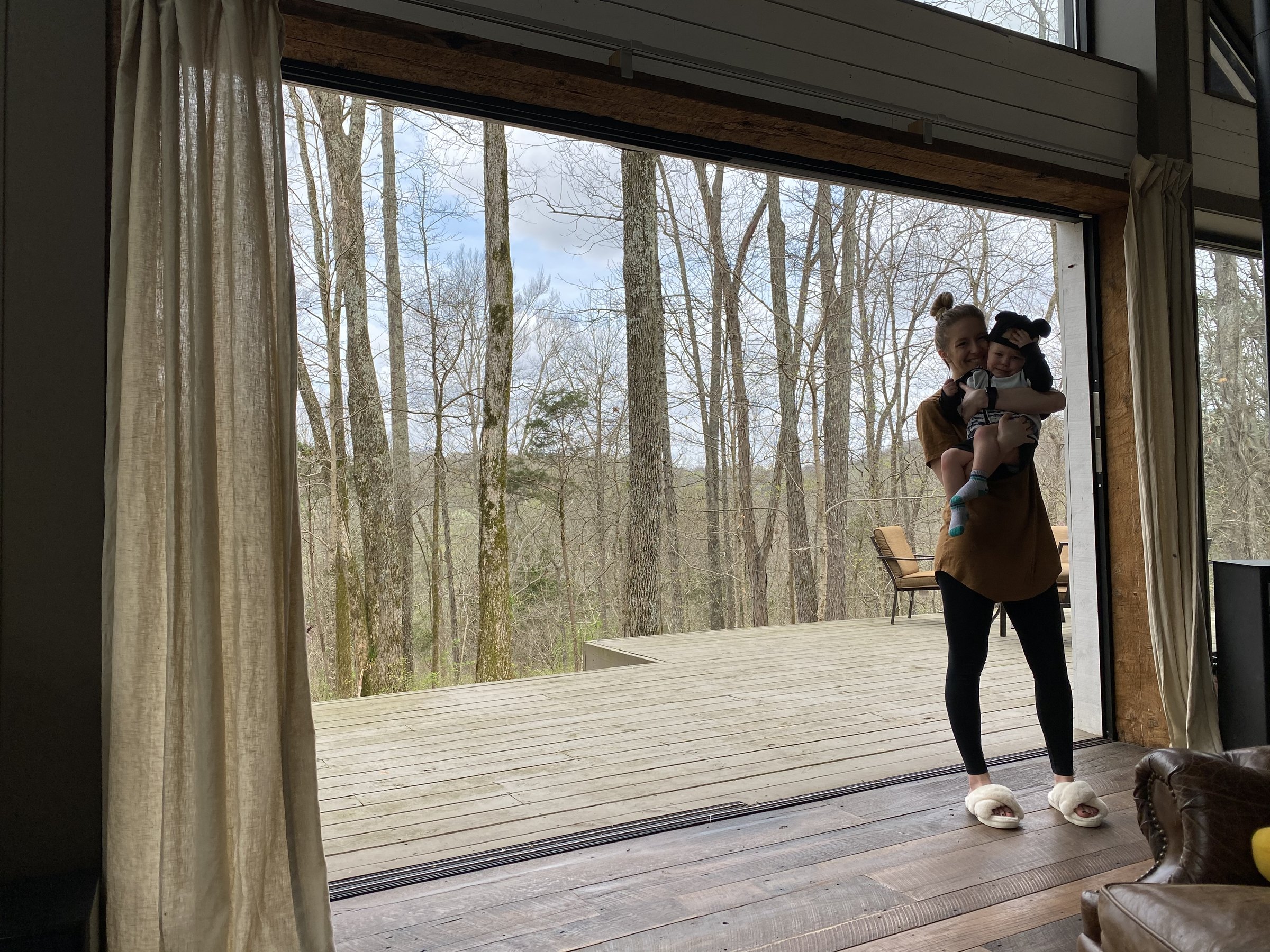 Liz holding her toddler in a doorway opening onto a wooden deck