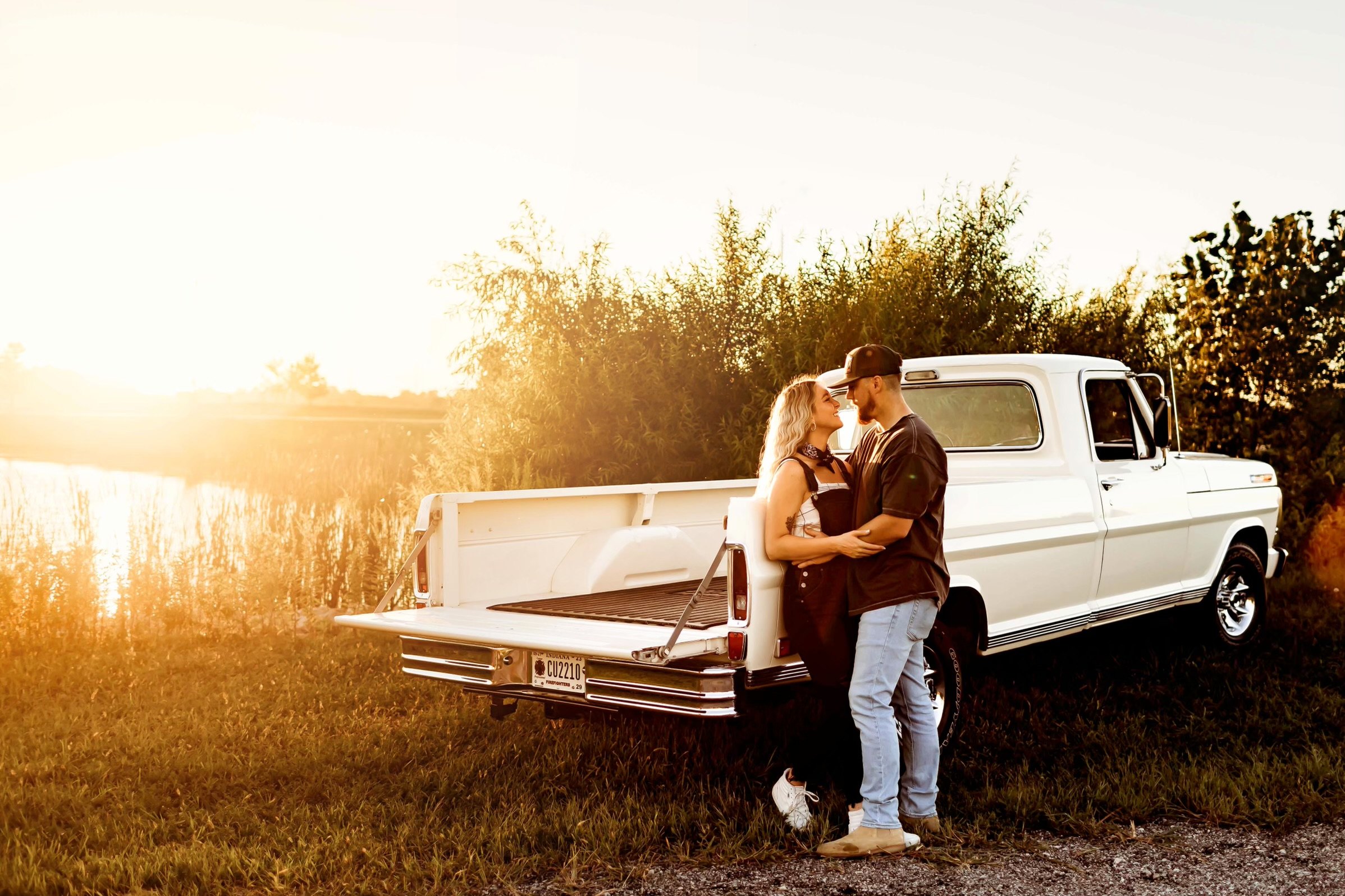 Liz and her husband beside a white vintage Ford pickup at golden hour by a lake in Indiana
