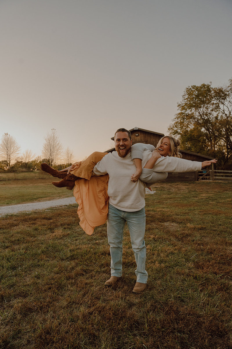 Liz and her husband laughing in front of a barn at golden hour