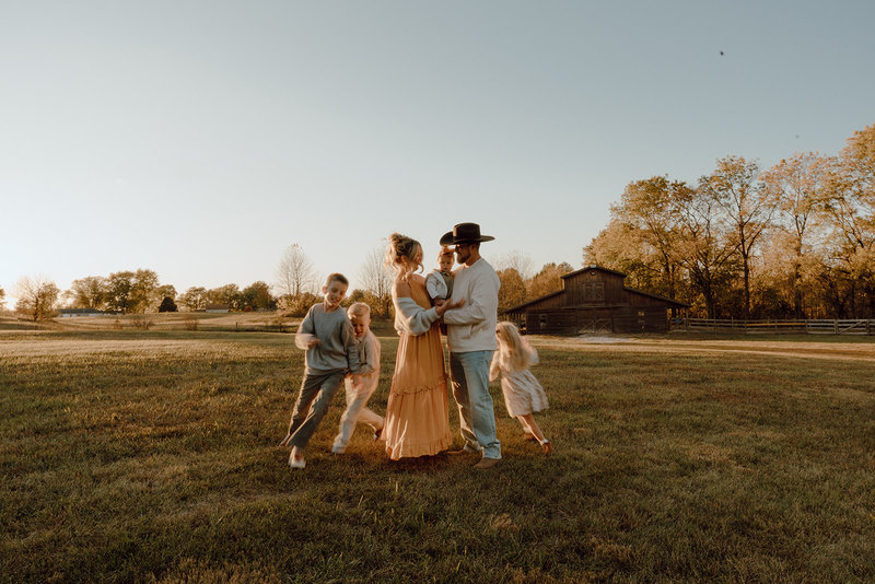 Liz and her family walking in a field in front of a barn at golden hour